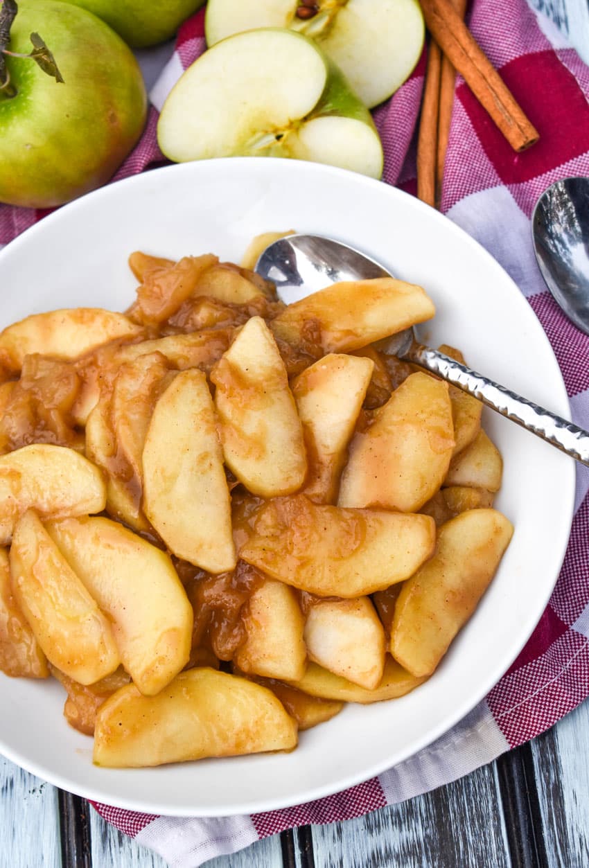 easy cinnamon apples in a shallow white bowl with a silver spoon on the side