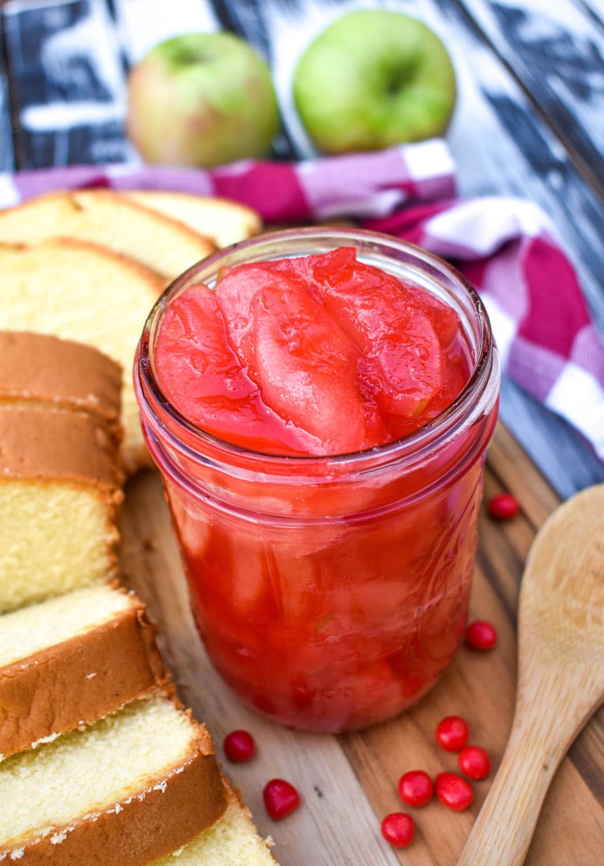 red hot cinnamon apples in a glass jar on a wooden cutting board