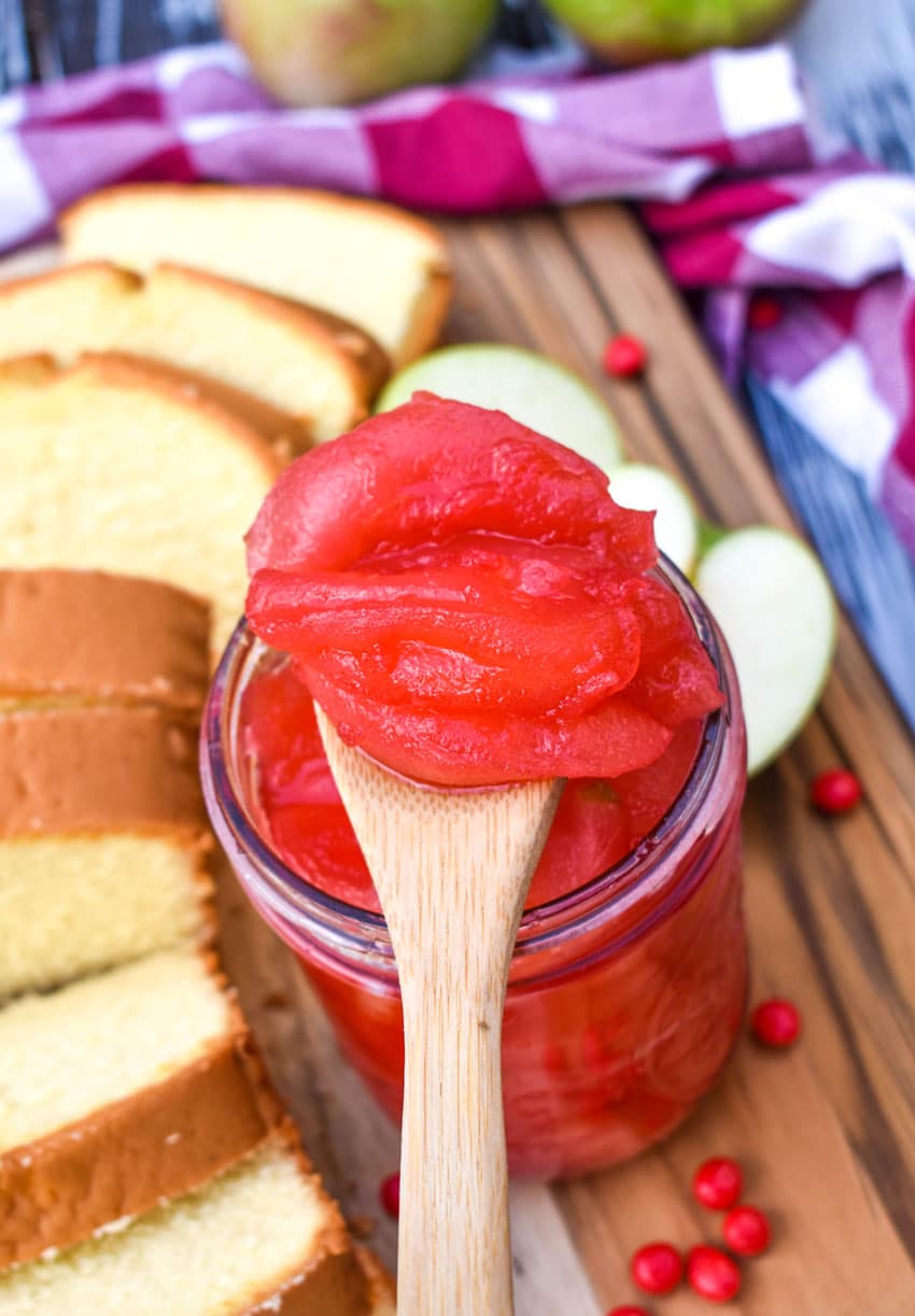 a wooden spoon resting on the edge of a glass jar holding a scoop of red hot cinnamon apples