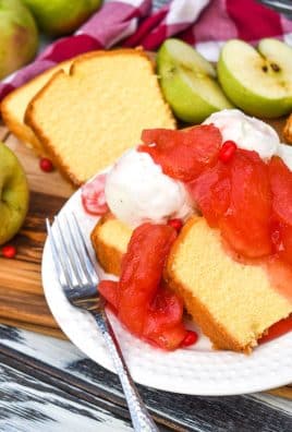 red hot cinnamon apples over slices of pound cake on a white plate with a silver fork on the side