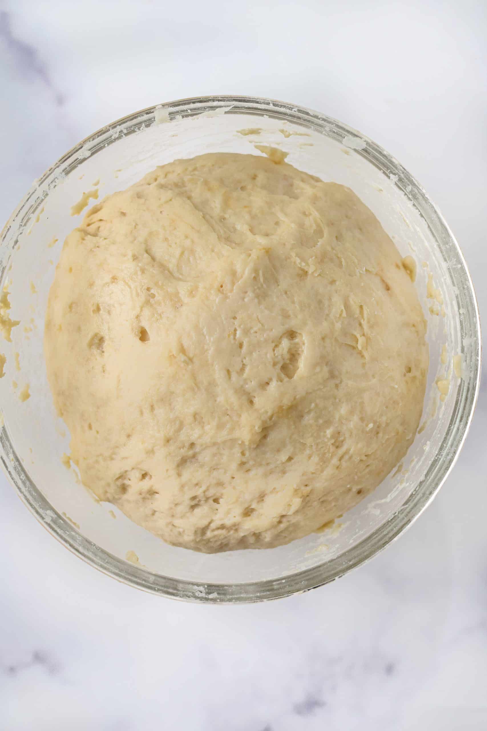 risen naan bread dough in a glass mixing bowl
