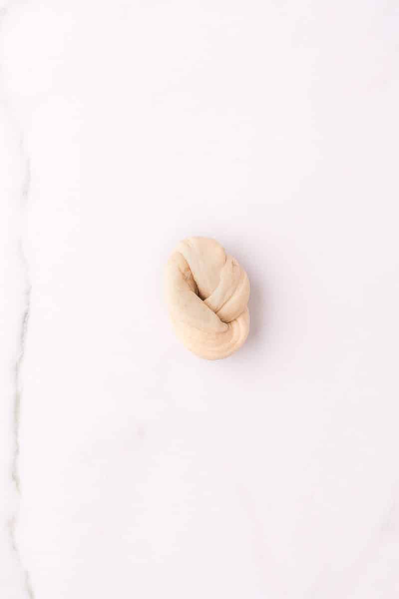 a strand of dough tied into a knot resting on a marble countertop