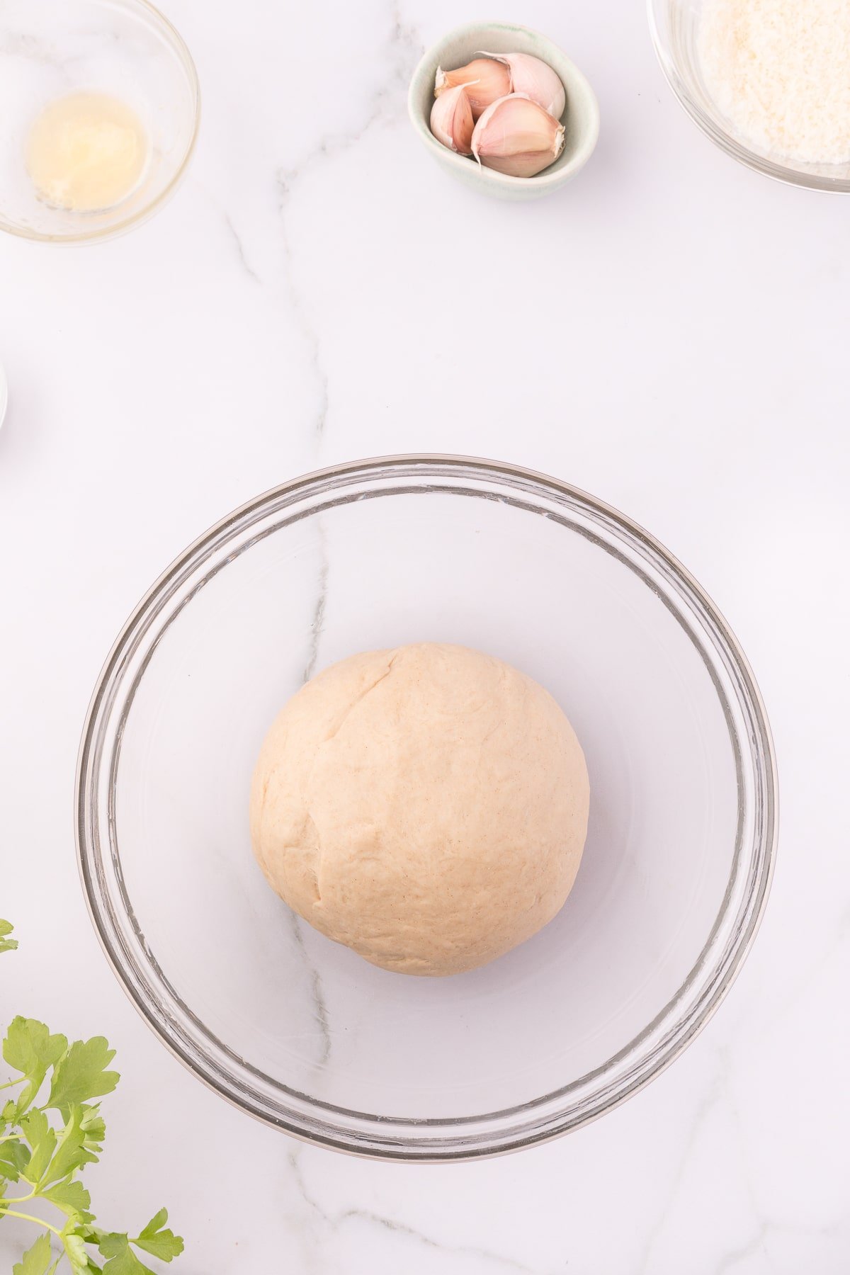 oiled dough ball resting in a glass mixing bowl
