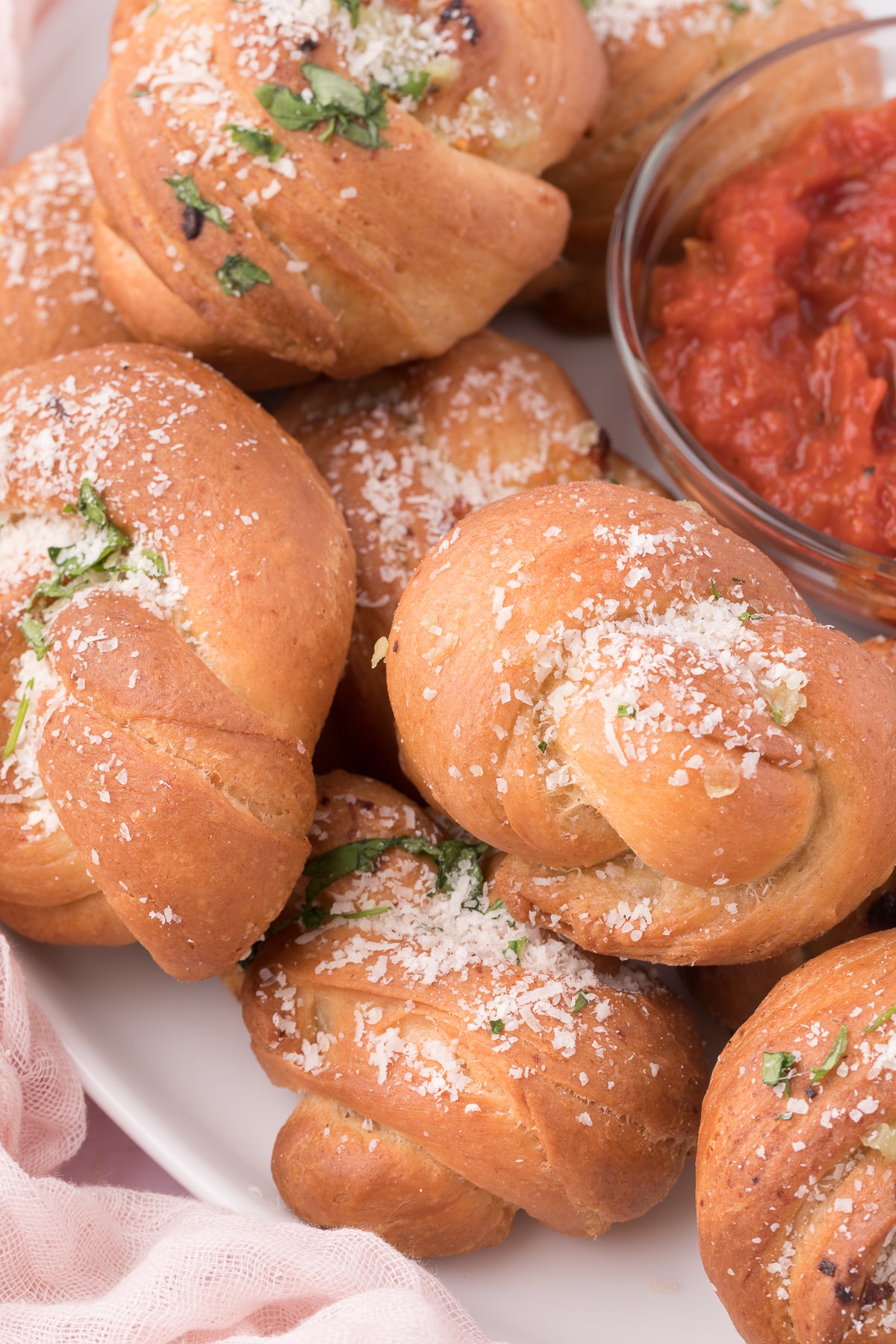 homemade garlic knots piled on a white serving plate around a small glass bowl filled with tomato dipping sauce