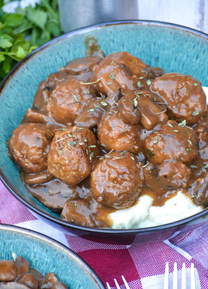 meatballs in mushroom gravy over mashed potatoes in a blue bowl
