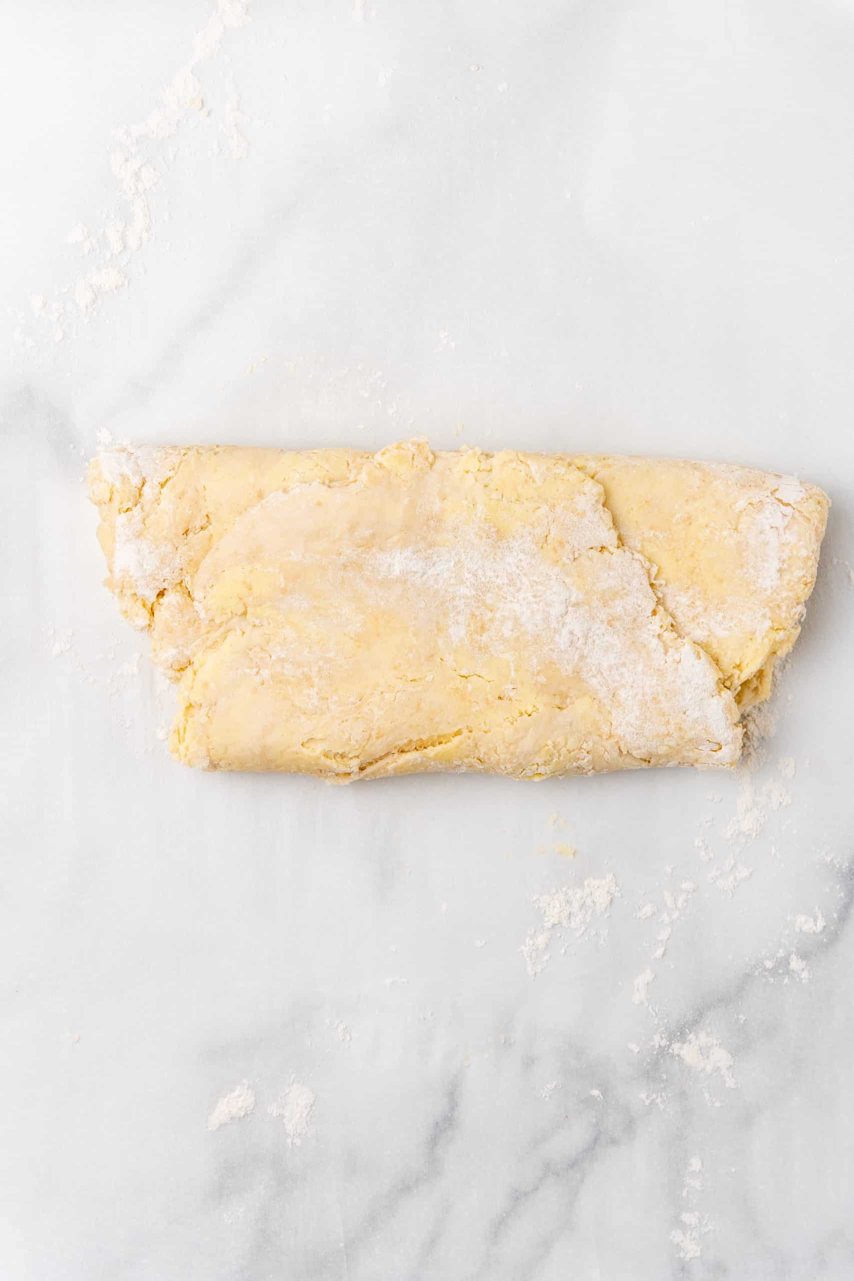 folded butter croissant dough on a floured marble countertop