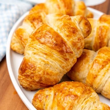homemade butter croissants stacked on a white plate
