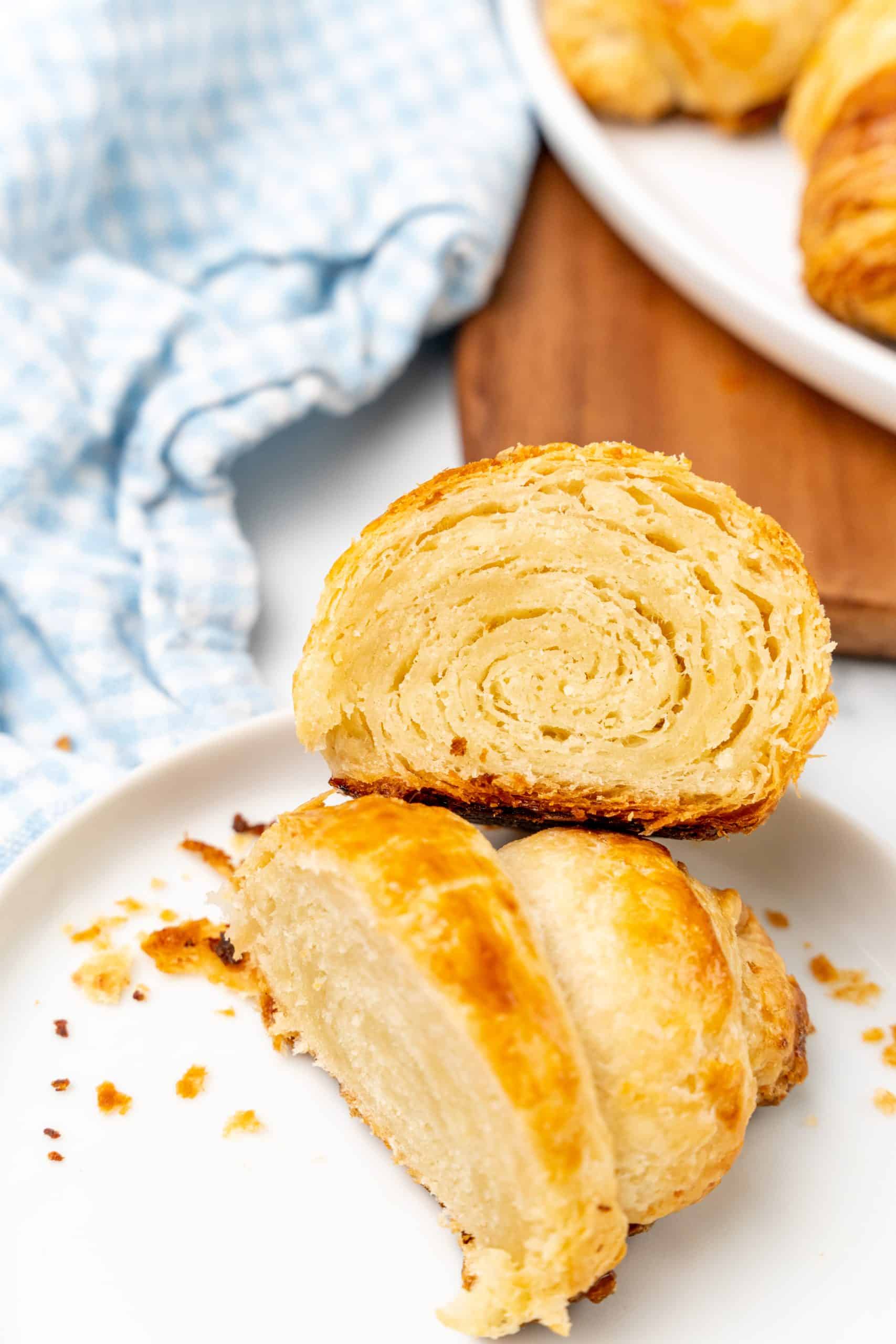 two halves of a flake homemade croissant roll resting on a small white plate
