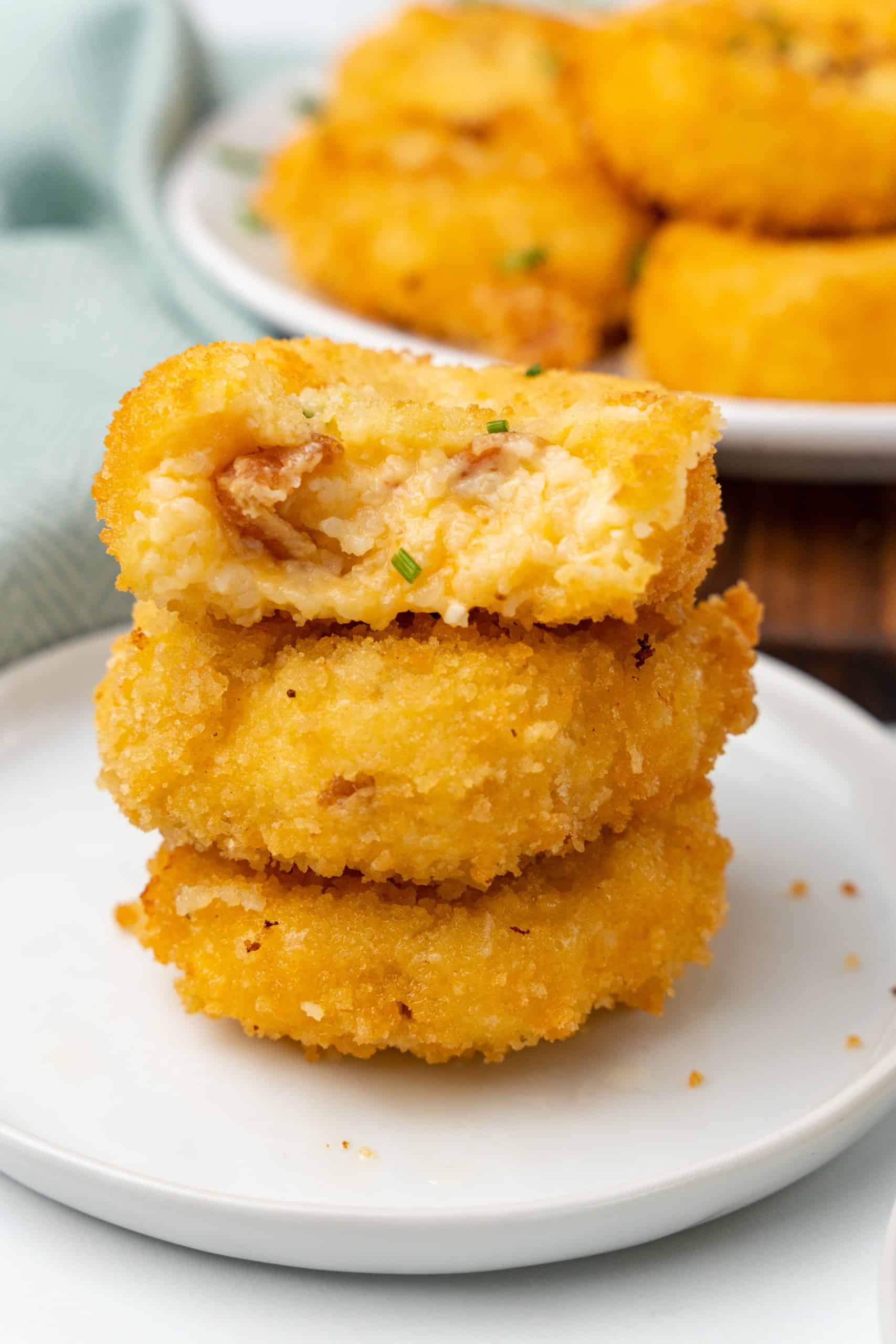 a stack of cheesy grit fritters on a small white plate with a bite removed from the top one
