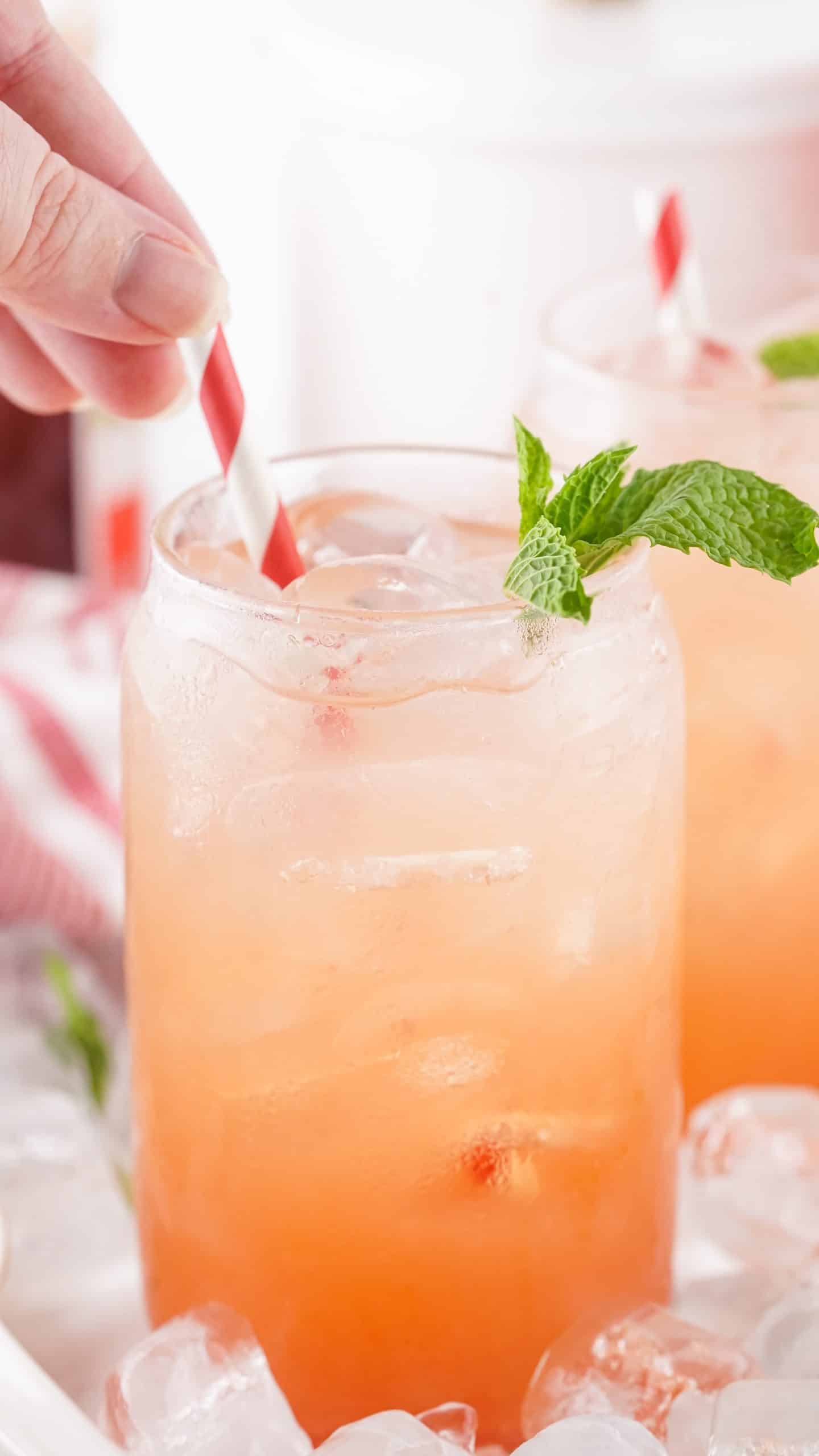 a hand sticking a striped paper straw in a glass filled with strawberry jam seltzer