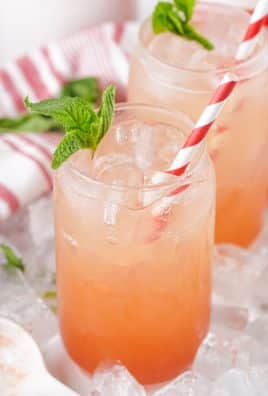 strawberry jam seltzer in two glass jars with fresh mint leaves and striped paper straws for garnish