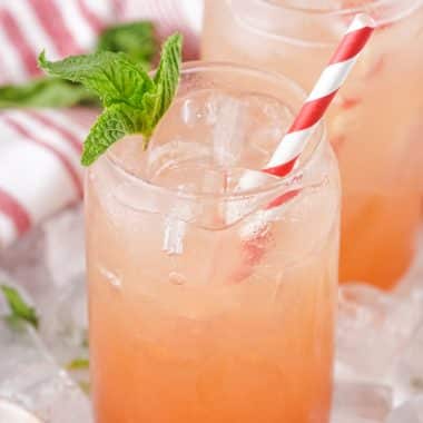 strawberry jam seltzer in two glass jars with fresh mint leaves and striped paper straws for garnish