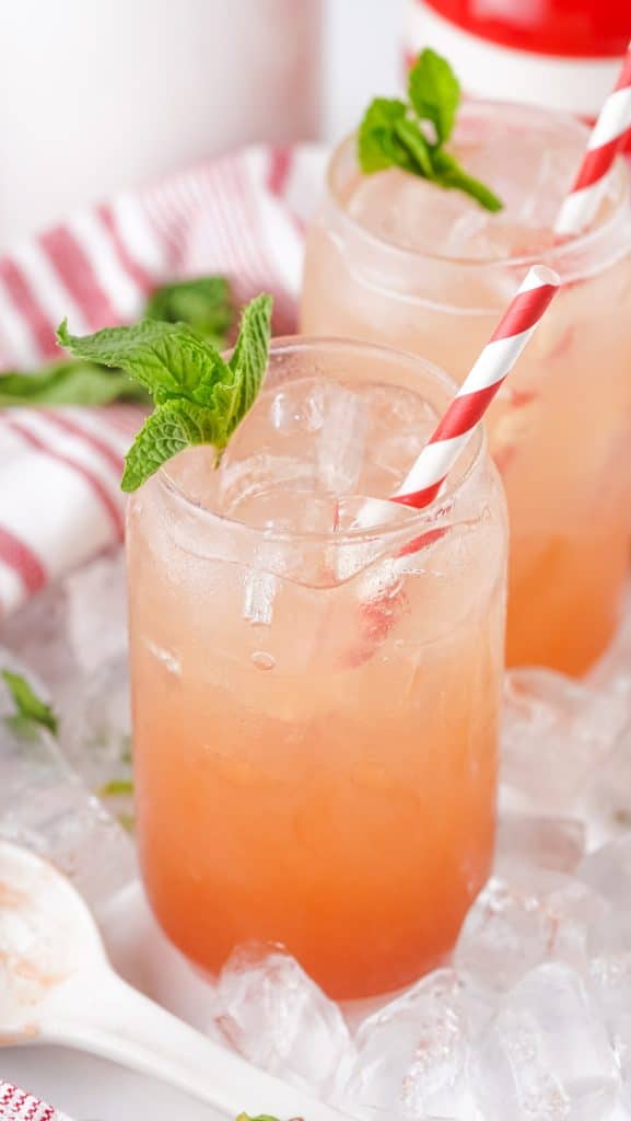 strawberry jam seltzer in two glass jars with fresh mint leaves and striped paper straws for garnish