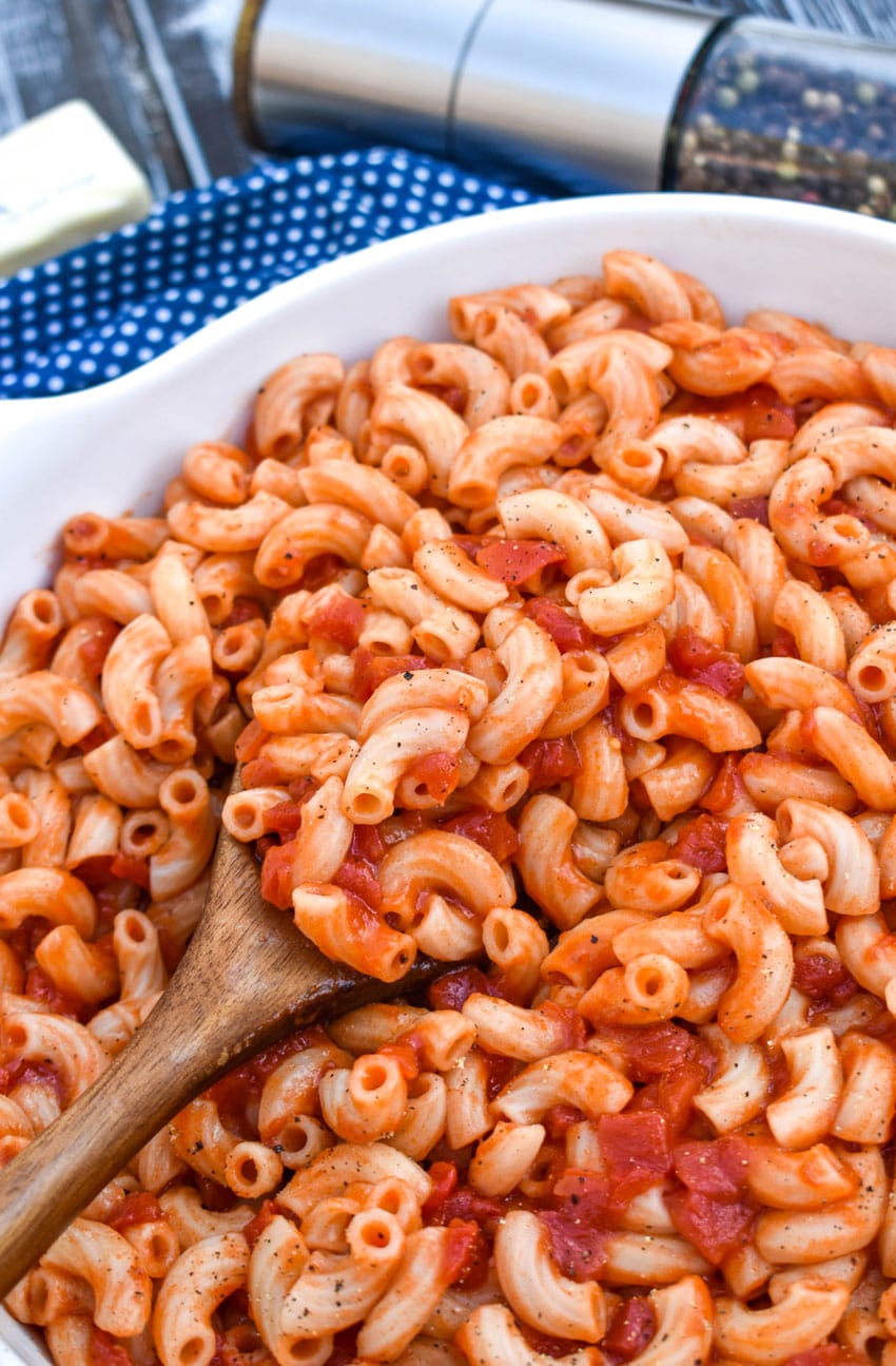 a wooden spoon in a white bowl filled with southern macaroni and tomatoes