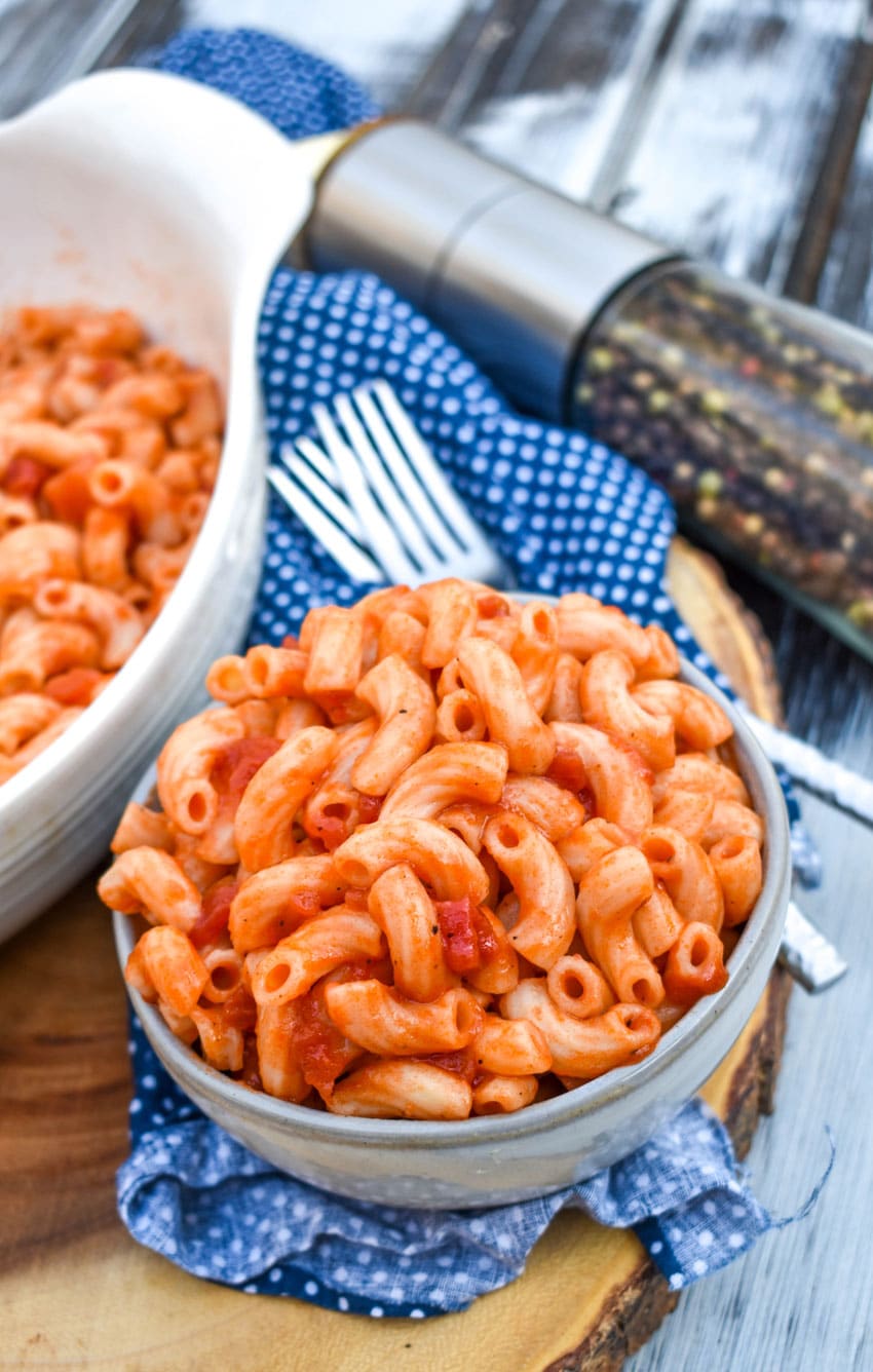 macaroni and tomatoes in a small gray bowl sitting on a wooden cutting board