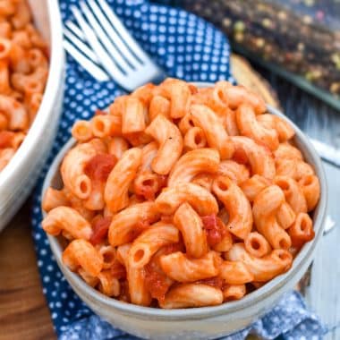 macaroni and tomatoes in a small gray bowl sitting on a wooden cutting board