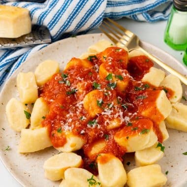 easy ricotta gnocchi on a speckled white plate topped with red sauce, herbs, and cheese