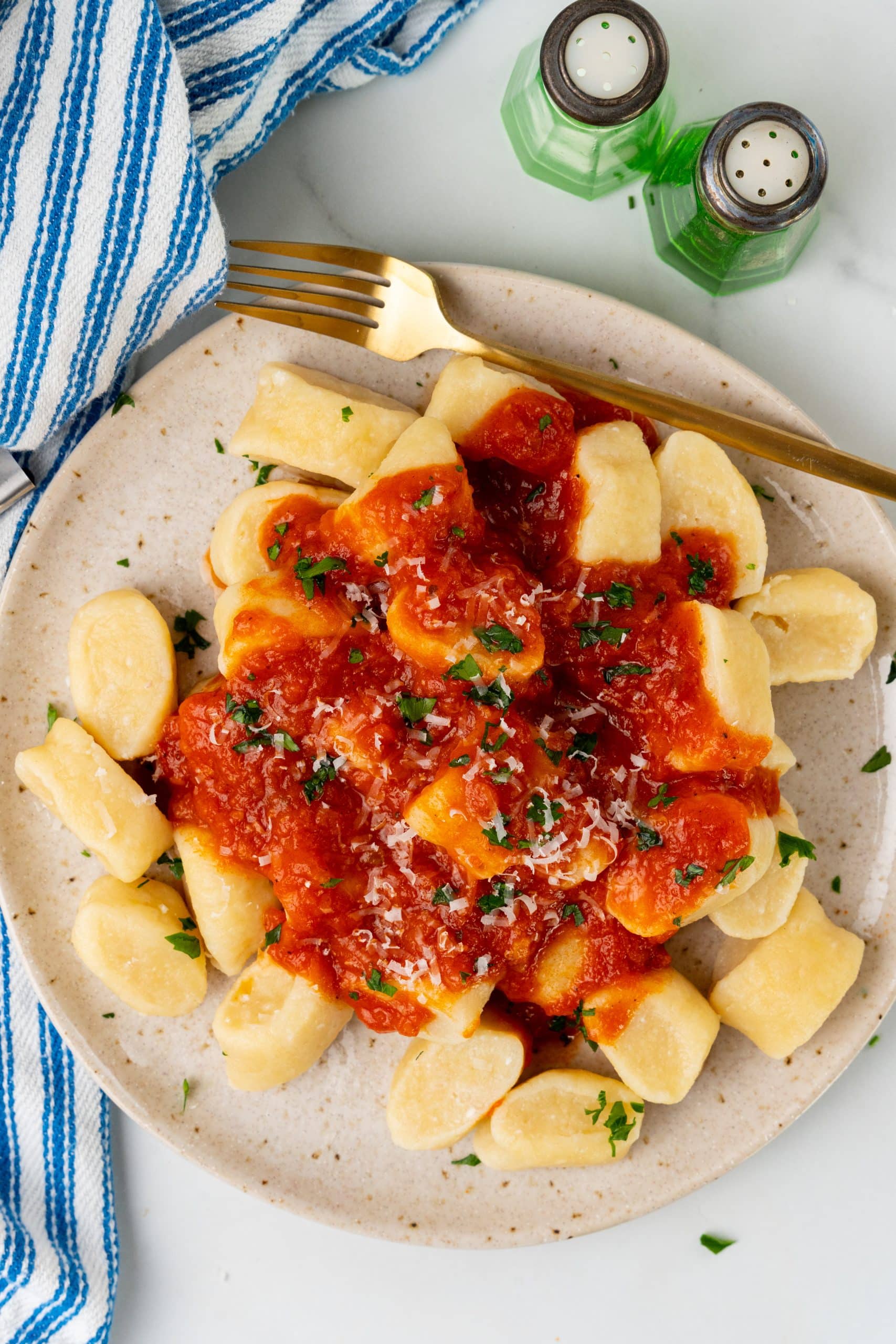 easy ricotta gnocchi on a speckled white plate topped with red sauce, herbs, and cheese