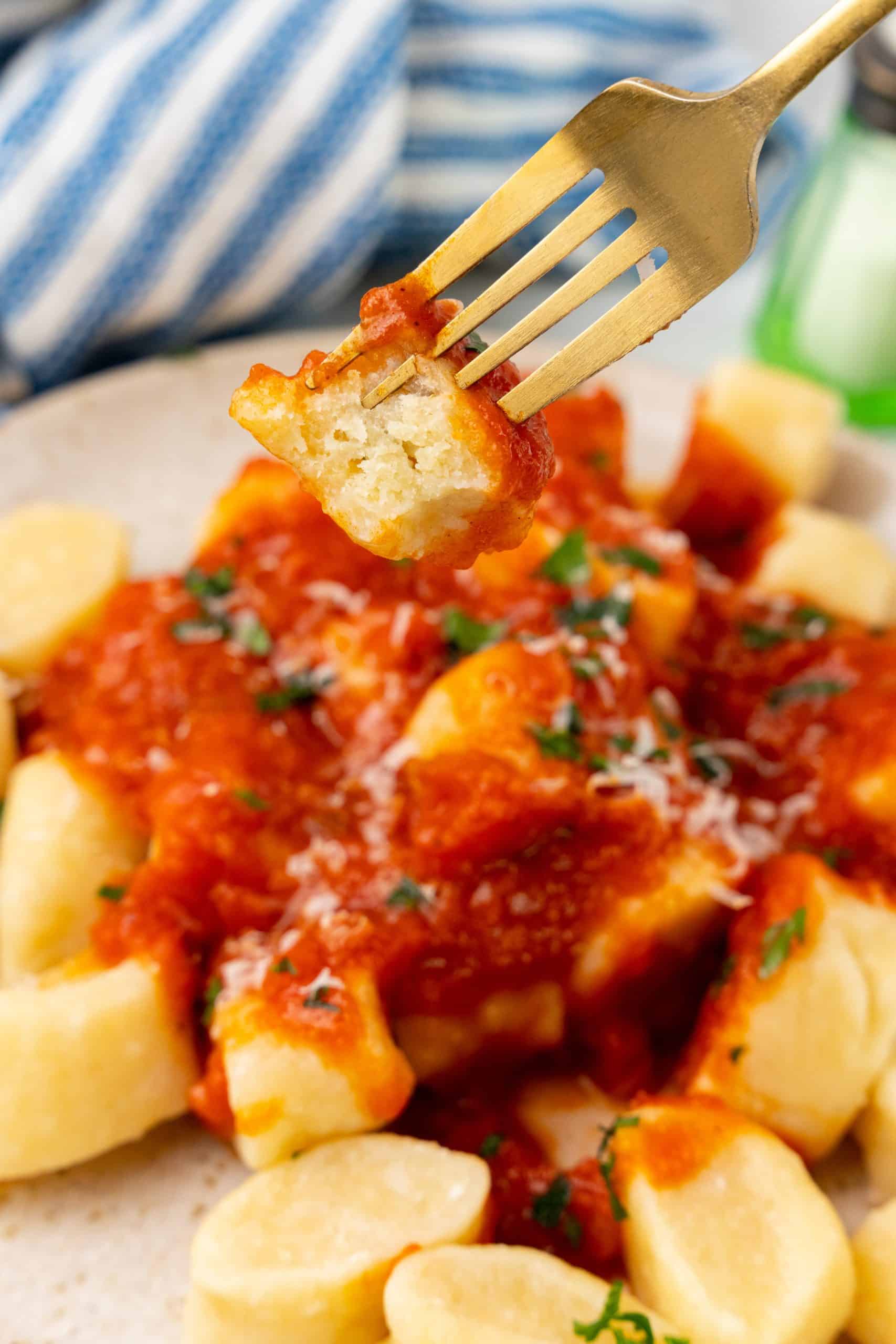 a gold fork holding up a sauce covered bitten piece of cooked gnocchi