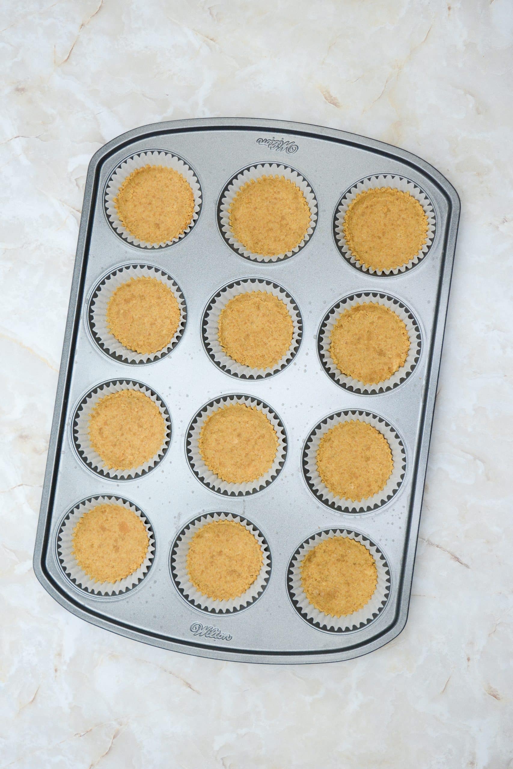 graham cracker crusts in cupcake liners in a muffin tin