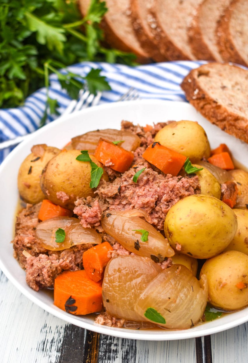 slow cooker corned beef hash in a white bowl with a slice of crusty bread on the side