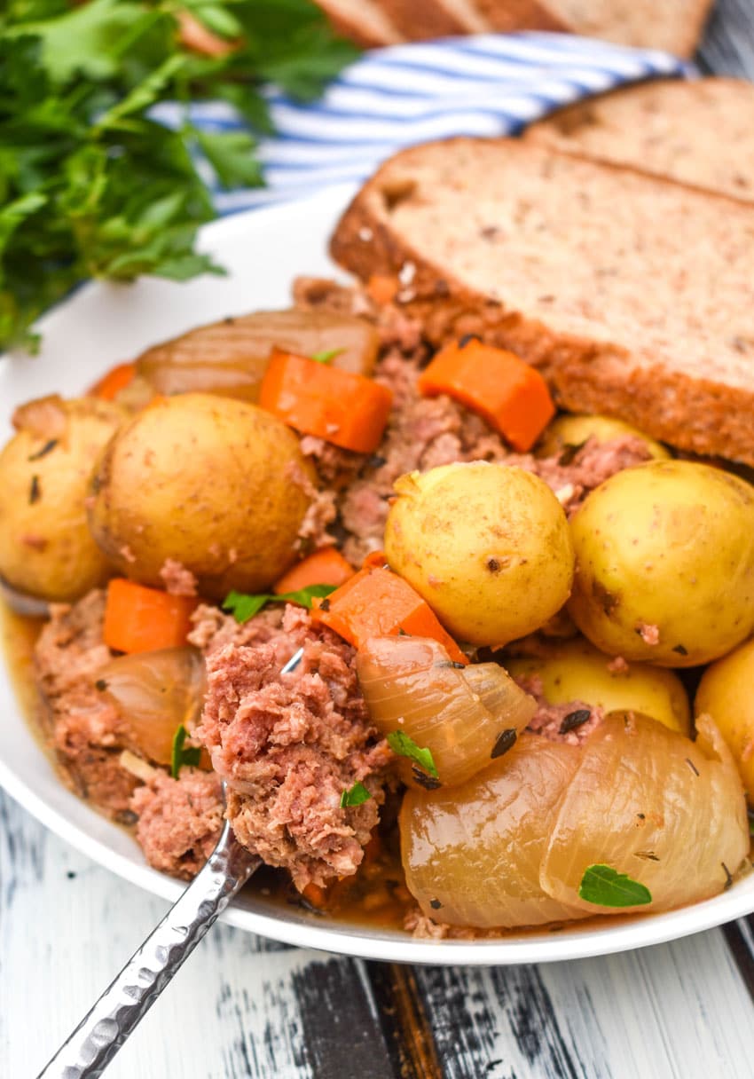 slow cooker corned beef hash in a white bowl with a slice of crusty bread on the side