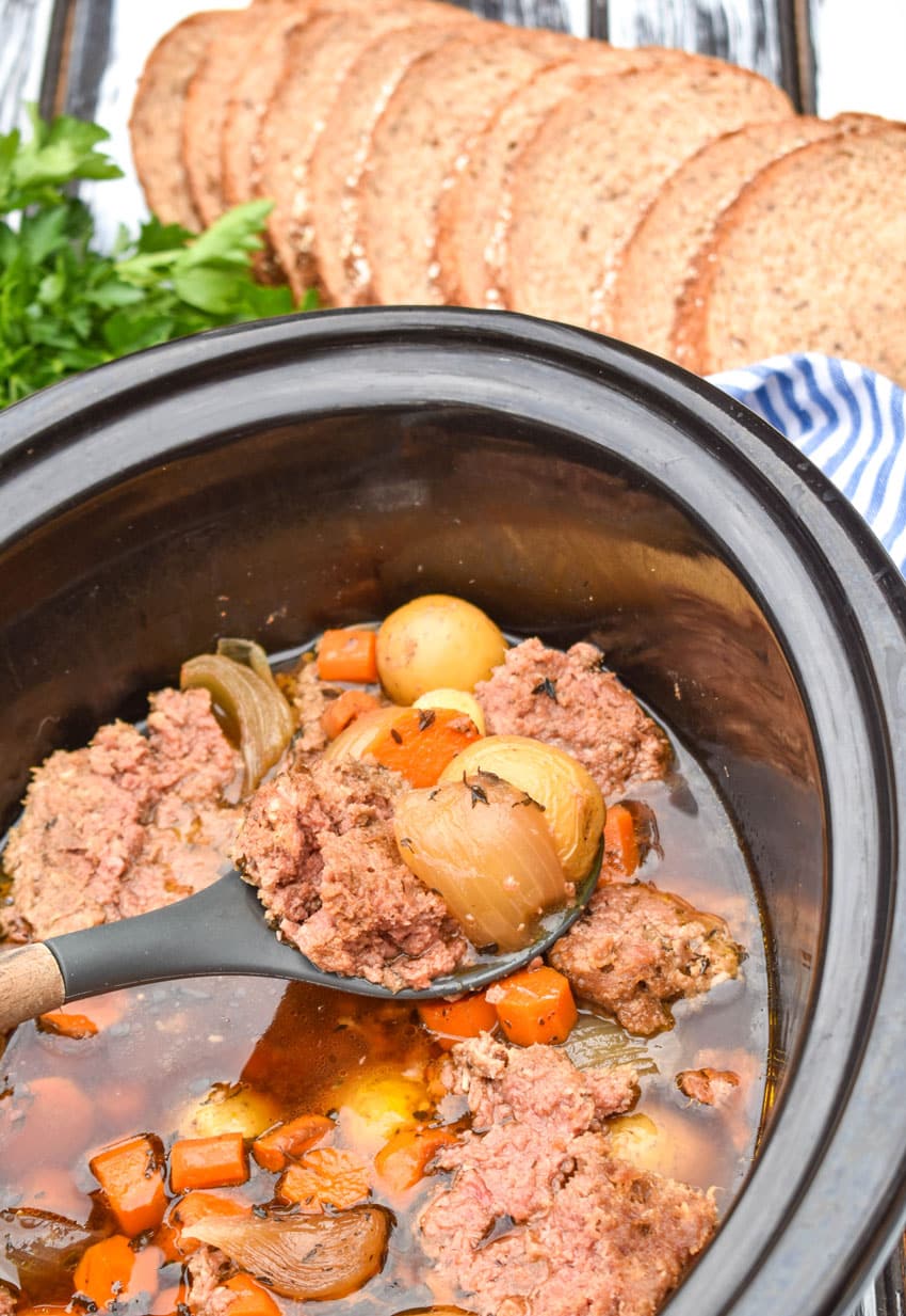 a spoon ladling slow cooker corned beef hash out of a black crock