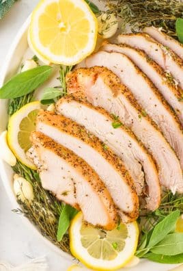 slices of a smoked turkey breast on a bed of fresh herbs and sliced lemons on a white platter