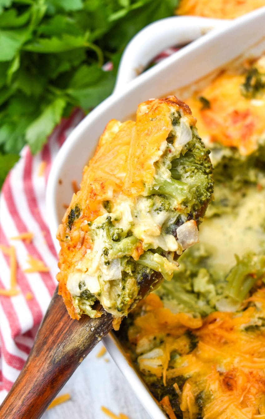 a wooden spoon holding up a scoop of easy cheesy baked broccoli casserole