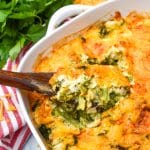 a wooden spoon in a casserole dish filled with cheesy broccoli souffle