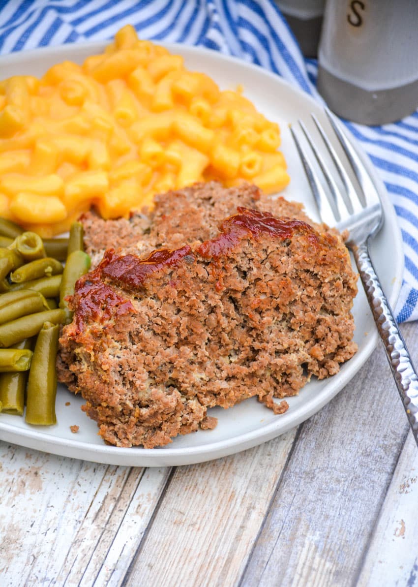 a slice of easy homemade meatloaf on a white dinner plate with mac and cheese and green beans on the side