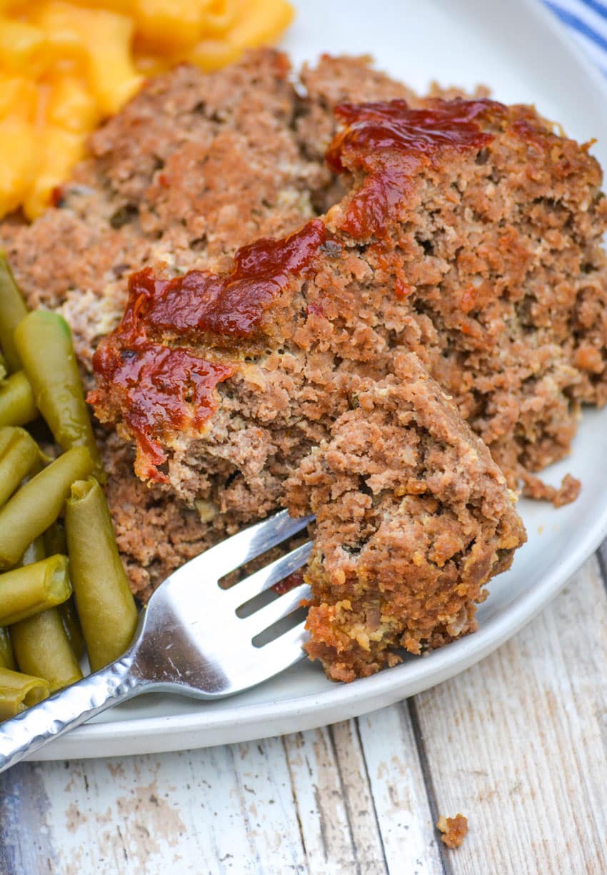 a silver fork on a white dinner plate with a slice of easy homemade meatloaf
