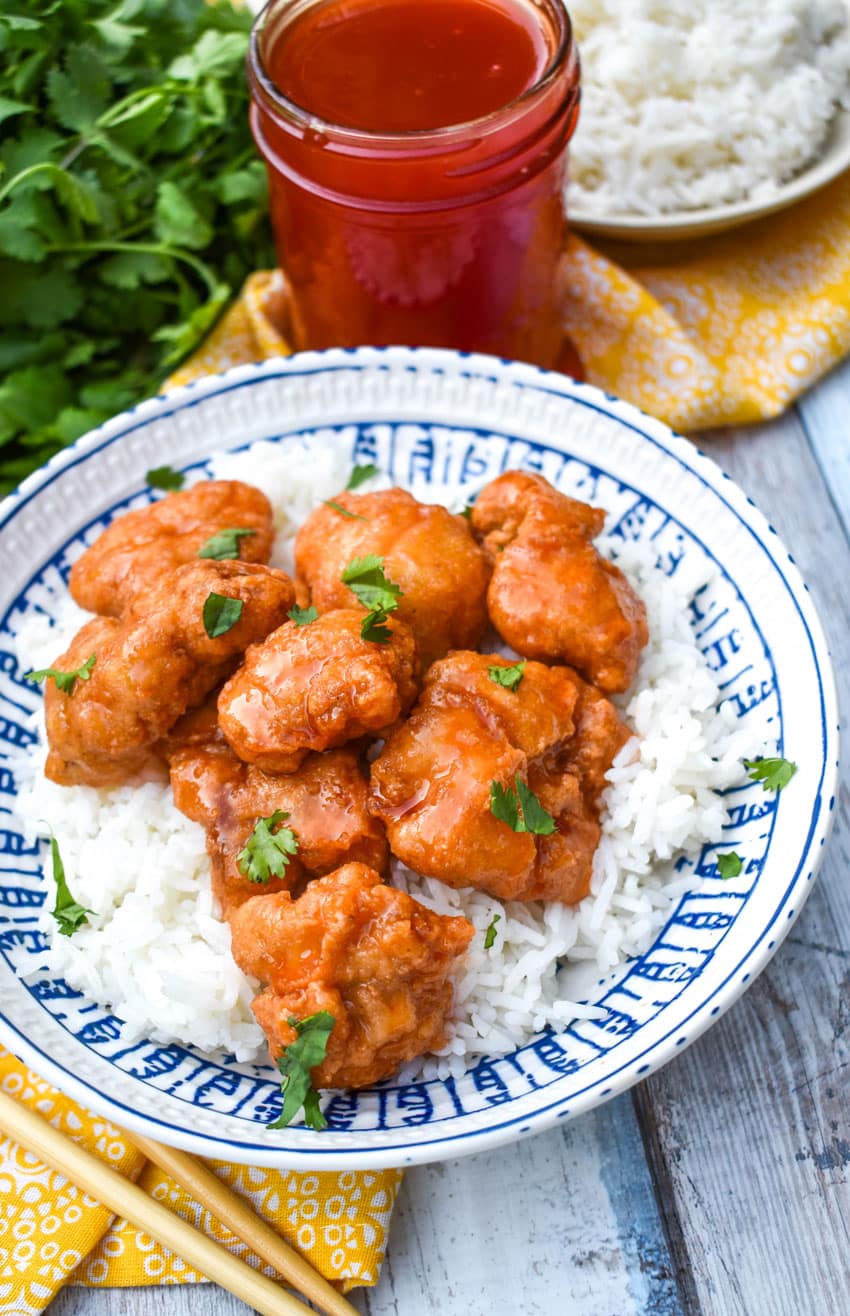 sweet and sour sauced chicken over white rice in a blue and white bowl
