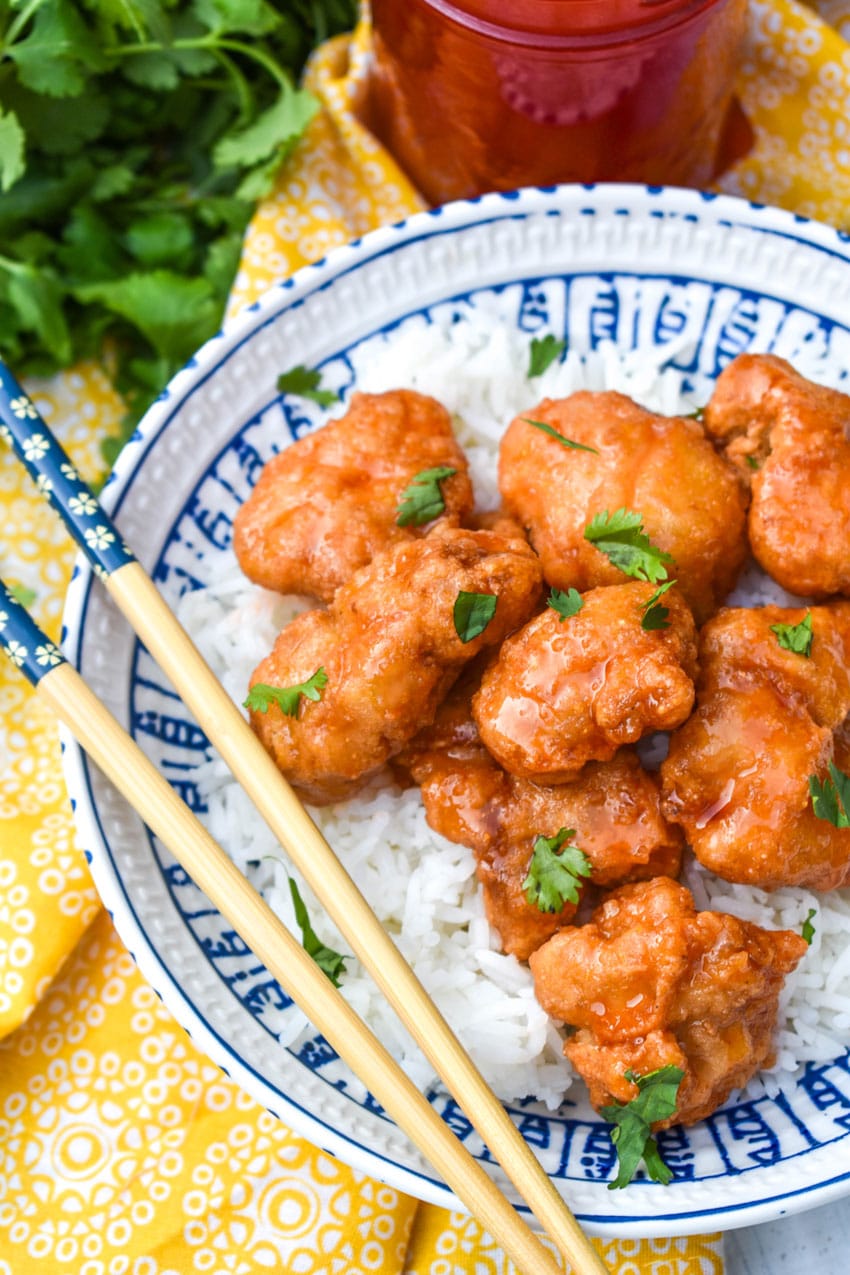 easy sweet and sour chicken over steamed white rice in a white and blue bowl with chopsticks resting on the edge