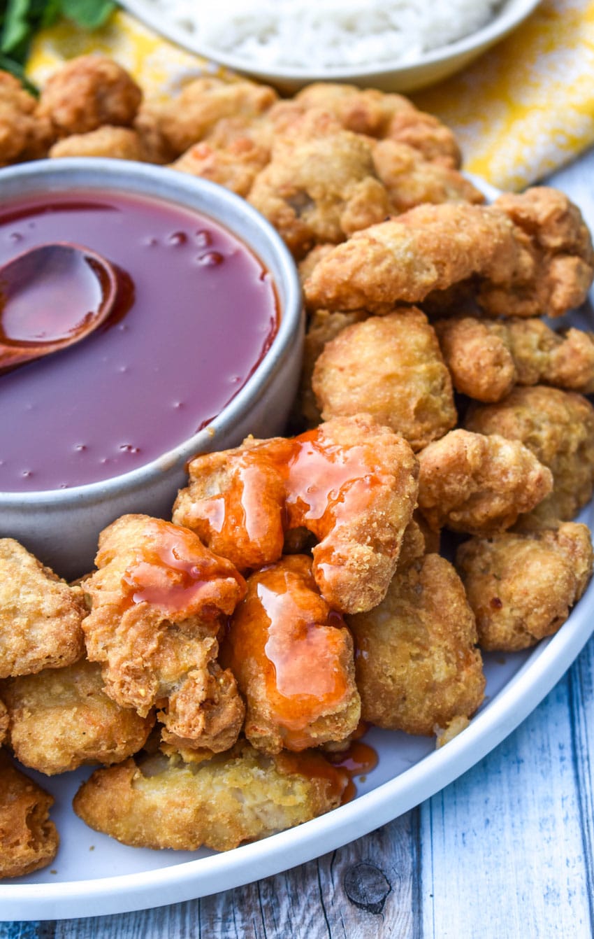 sweet and sour sauce poured over pieces of fried chicken on a white plate