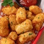 homemade tater tots in a red plastic basket with a cup of ketchup on the side