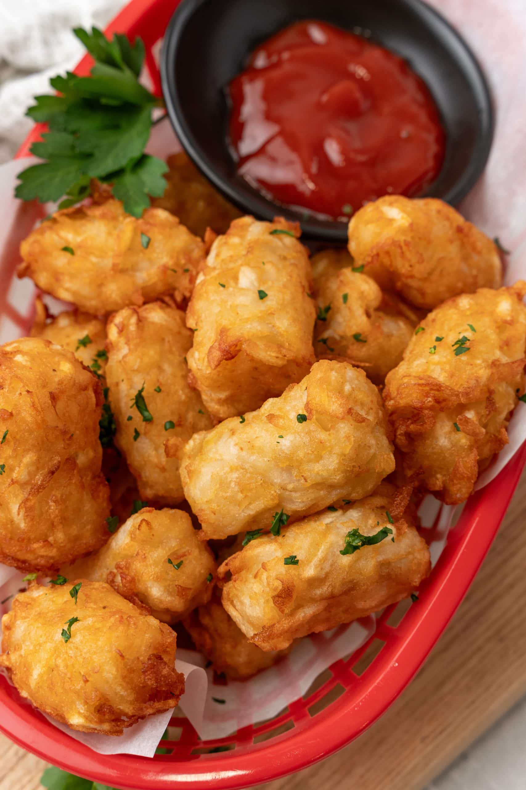 homemade tater tots in a red plastic basket with a cup of ketchup on the side