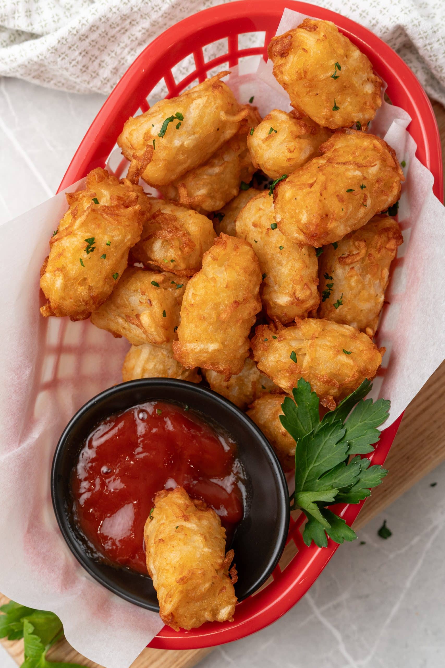 homemade tater tots in a red plastic basket with a cup of ketchup on the side
