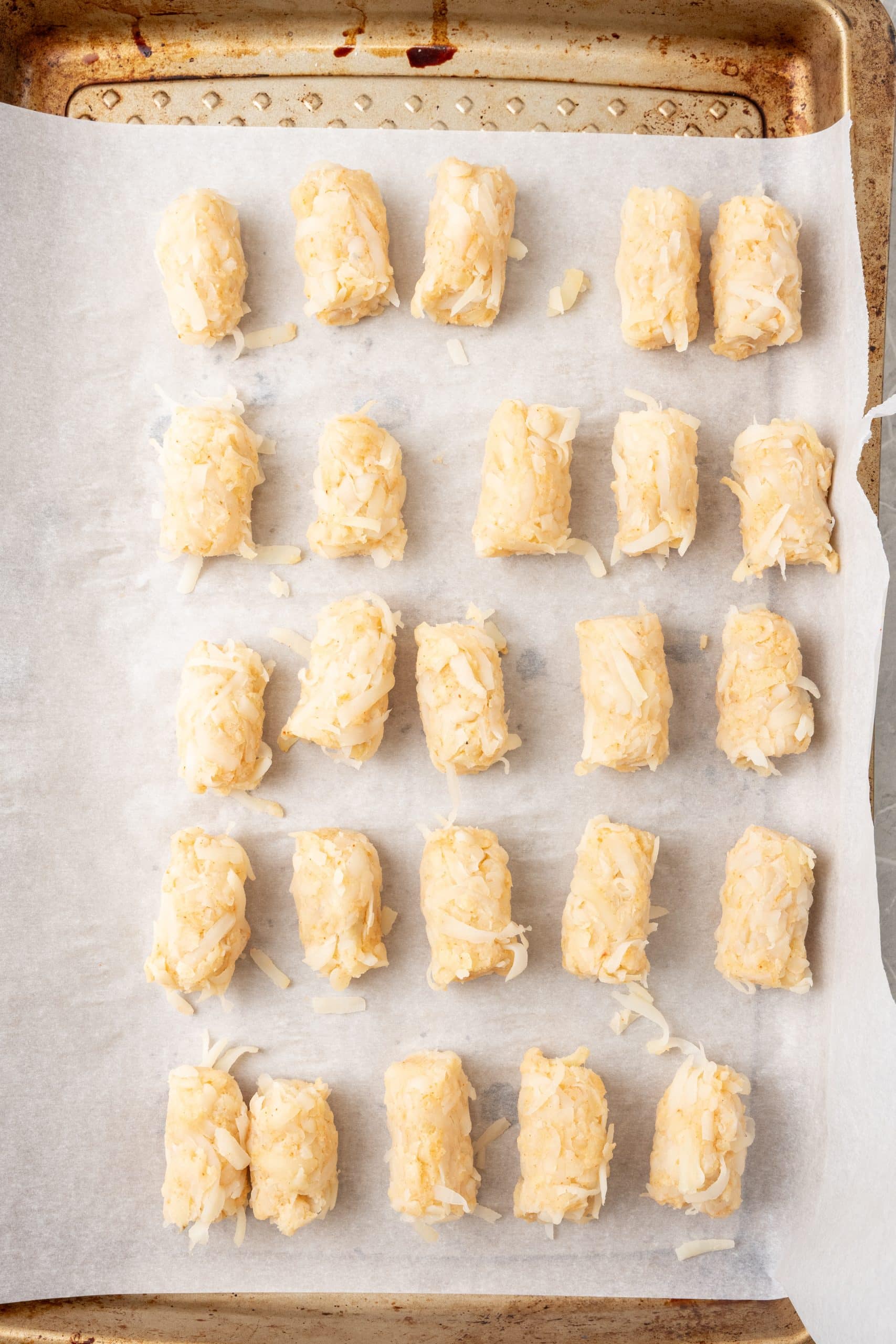 shredded potatoes shaped into tater tots and lined up on a parchment paper lined baking sheet