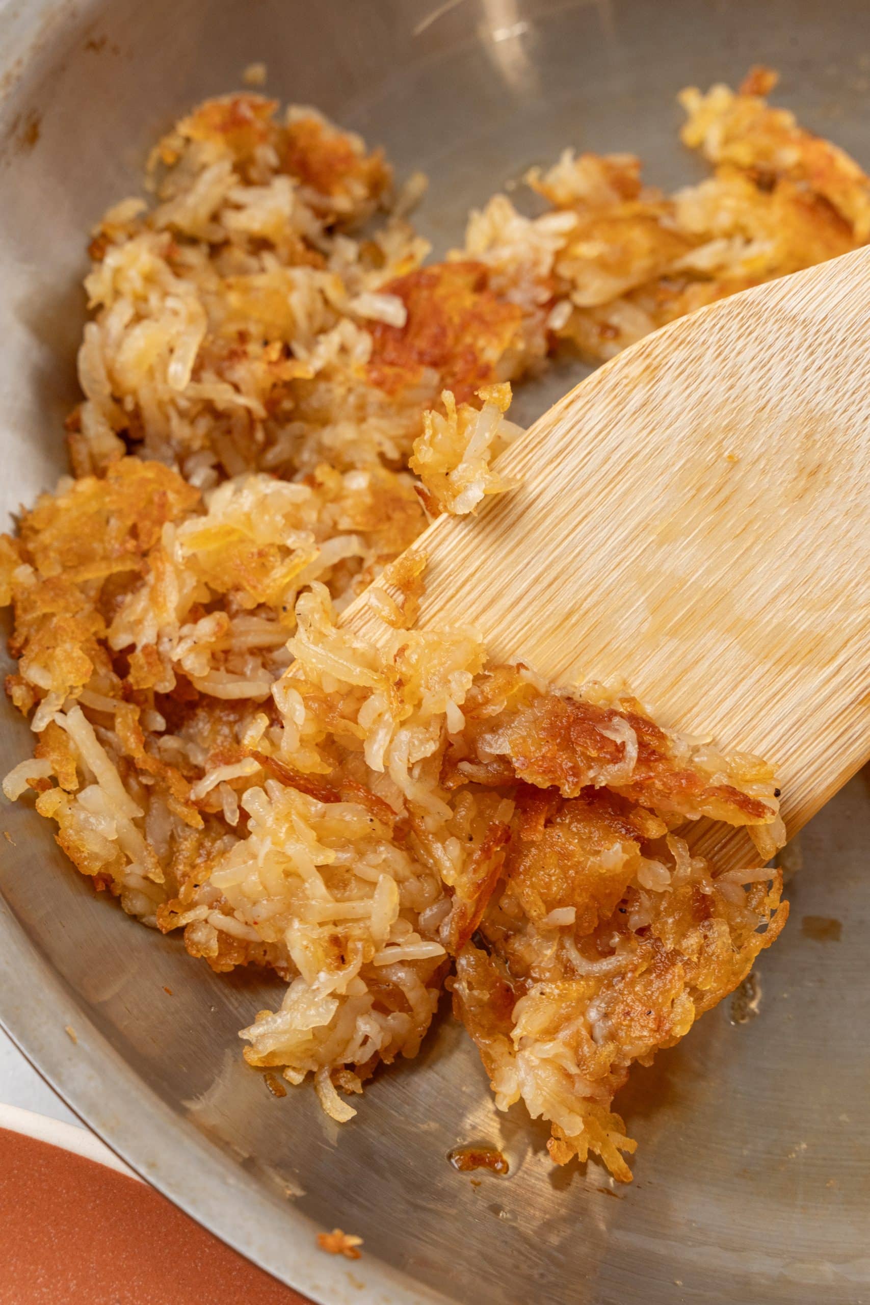 a wooden spatula stirring crispy golden hash browns in a silver skillet