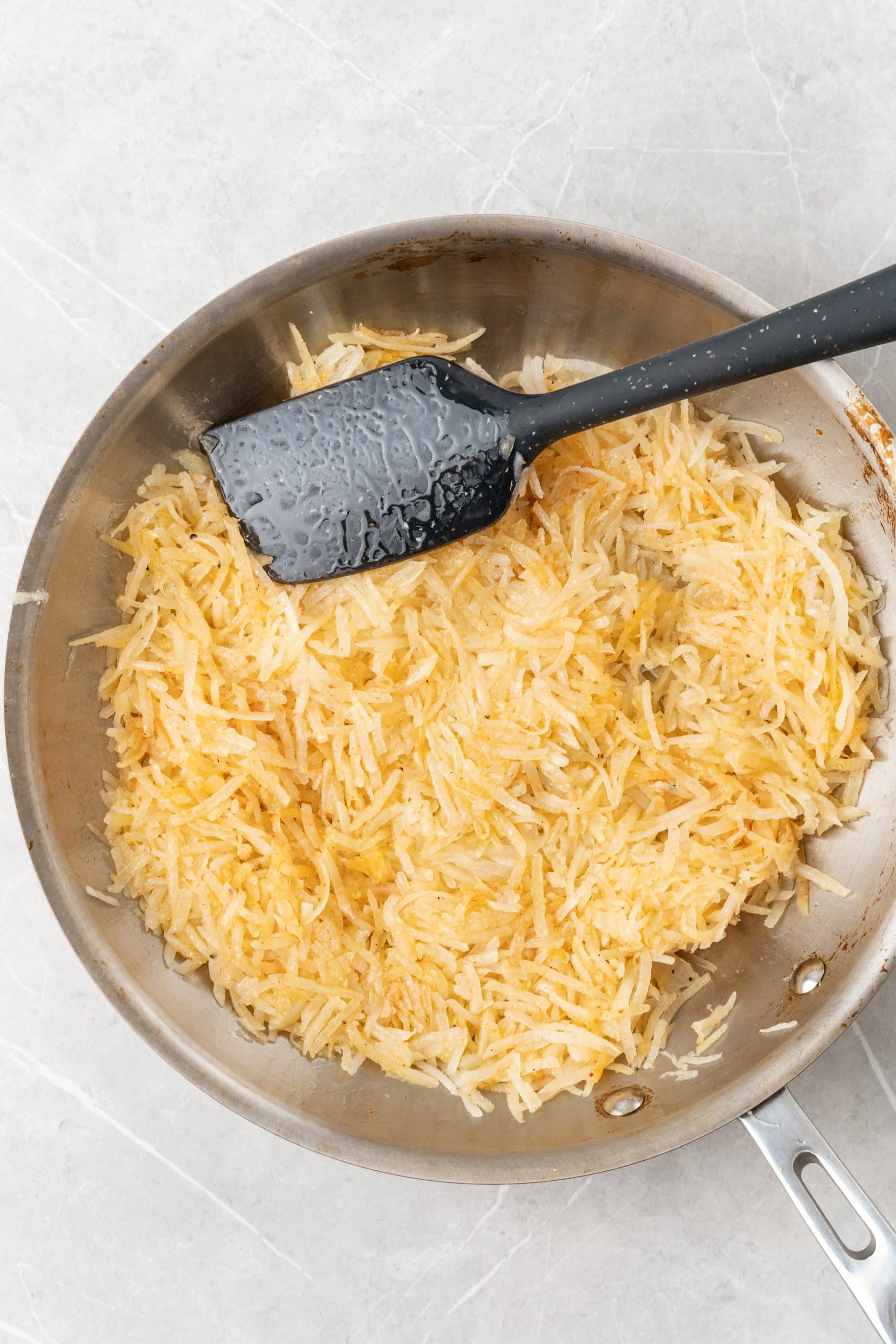 shredded hash browns browning in a silver skillet