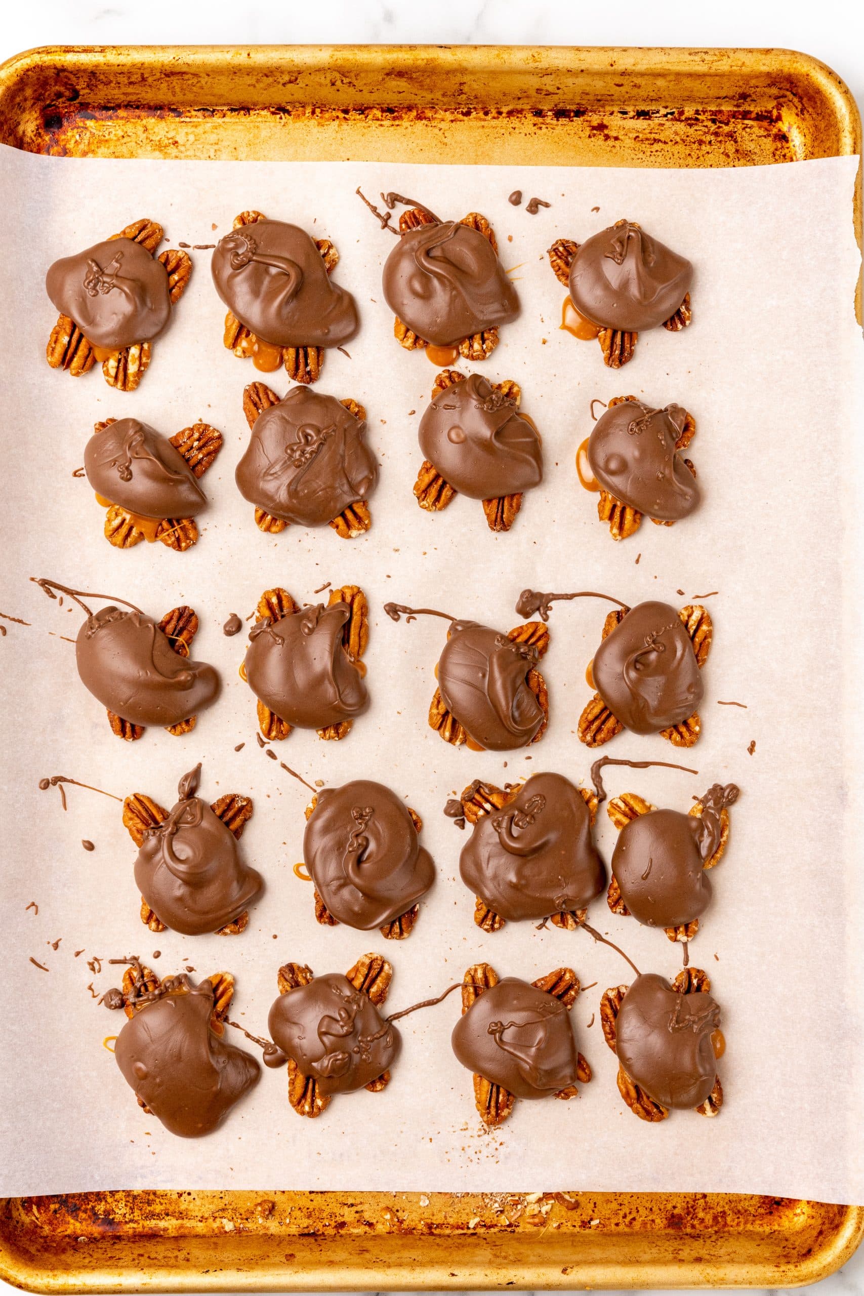 homemade chocolate turtles candy on a parchment paper lined baking sheet