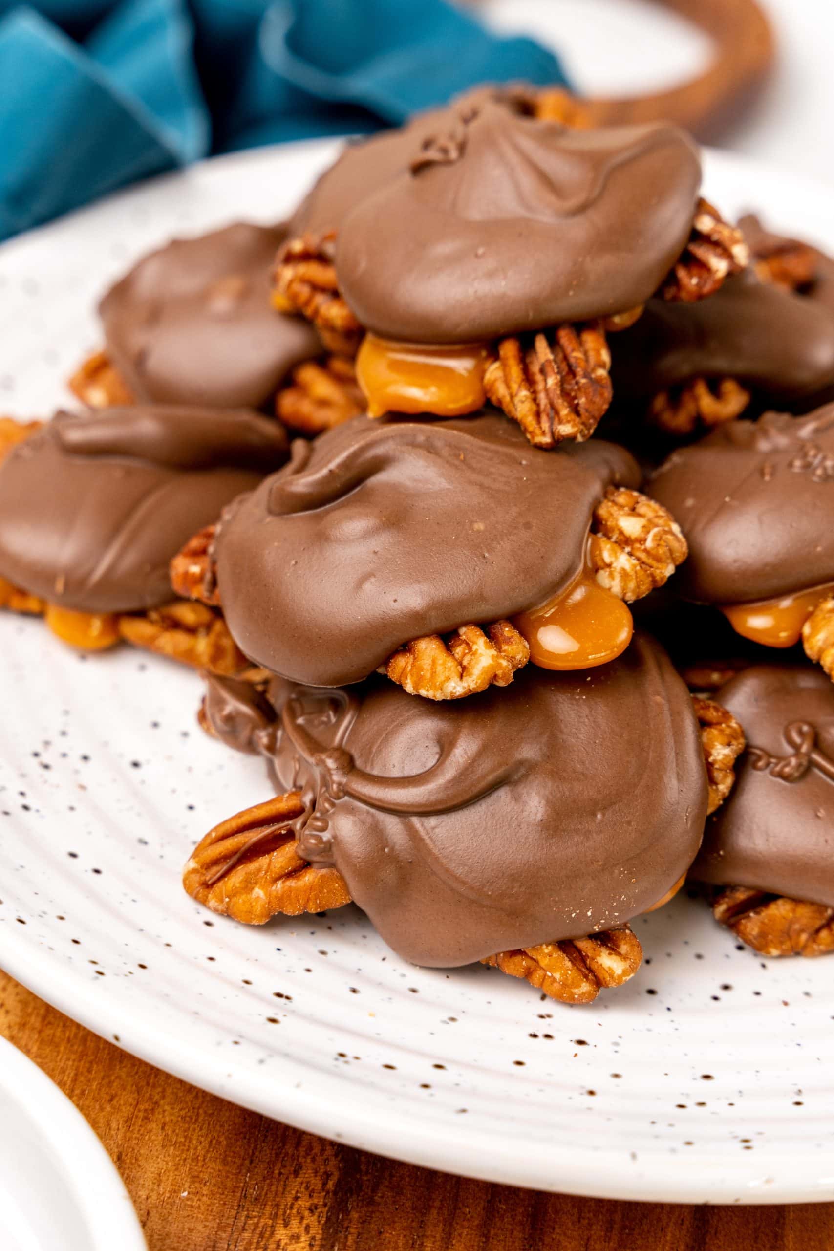 homemade chocolate turtles candy stacked on a white plate