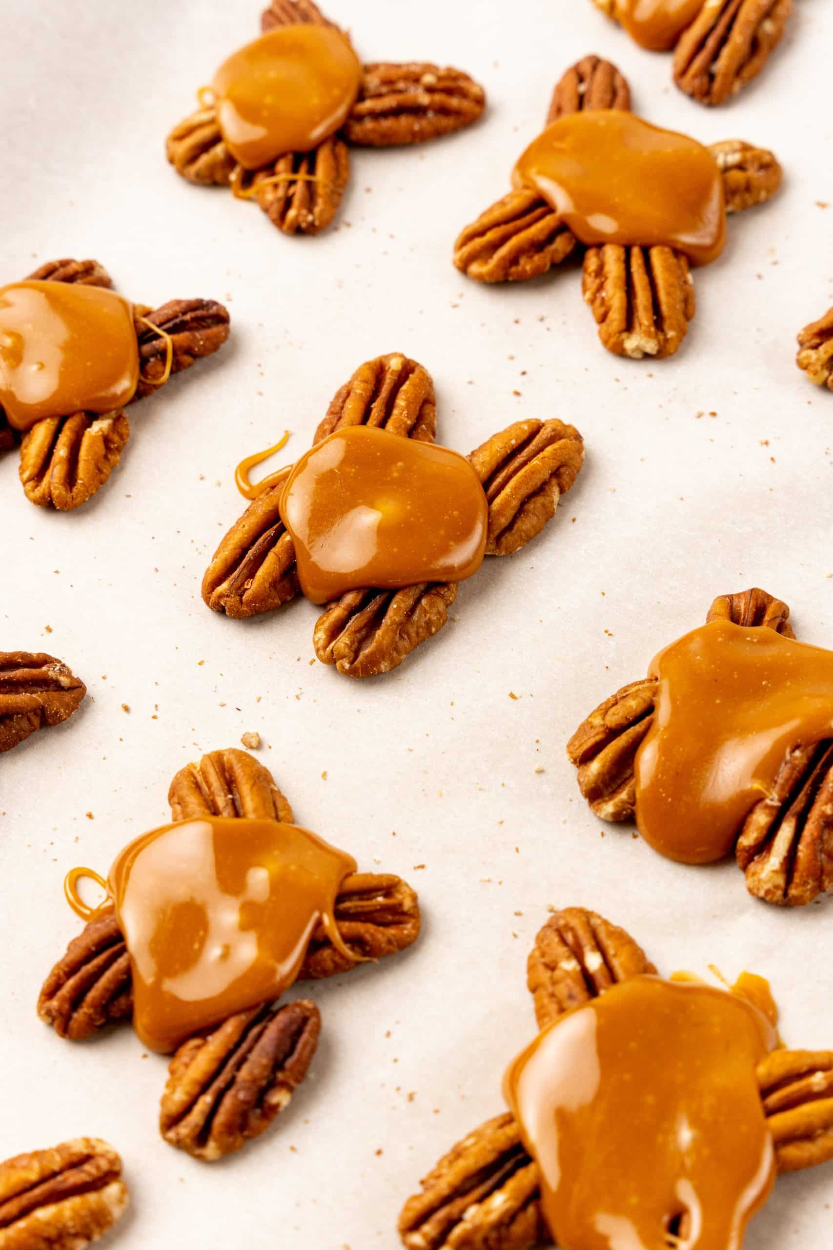 caramel poured over pecan halves arranged on a parchment paper lined baking sheet