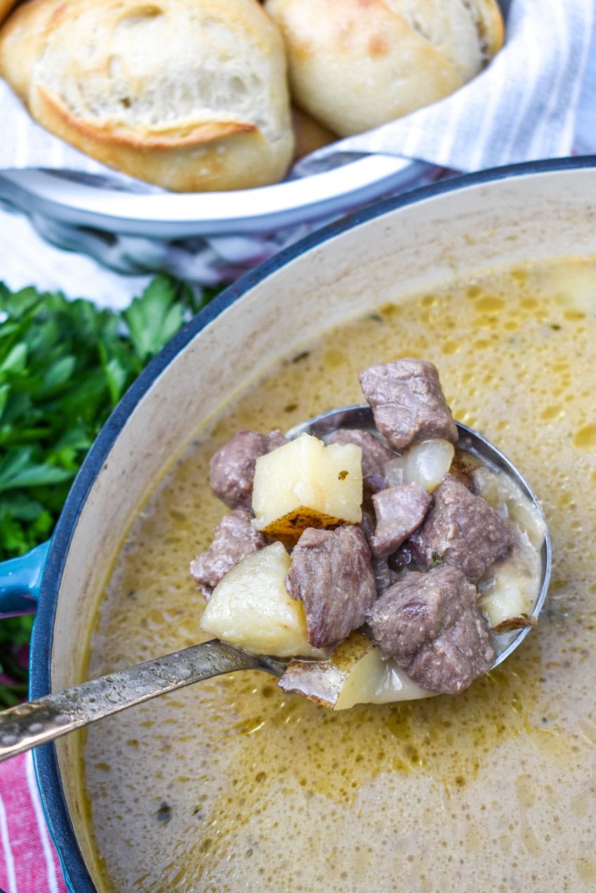a silver ladle scooping steak and potato soup out of a large dutch oven