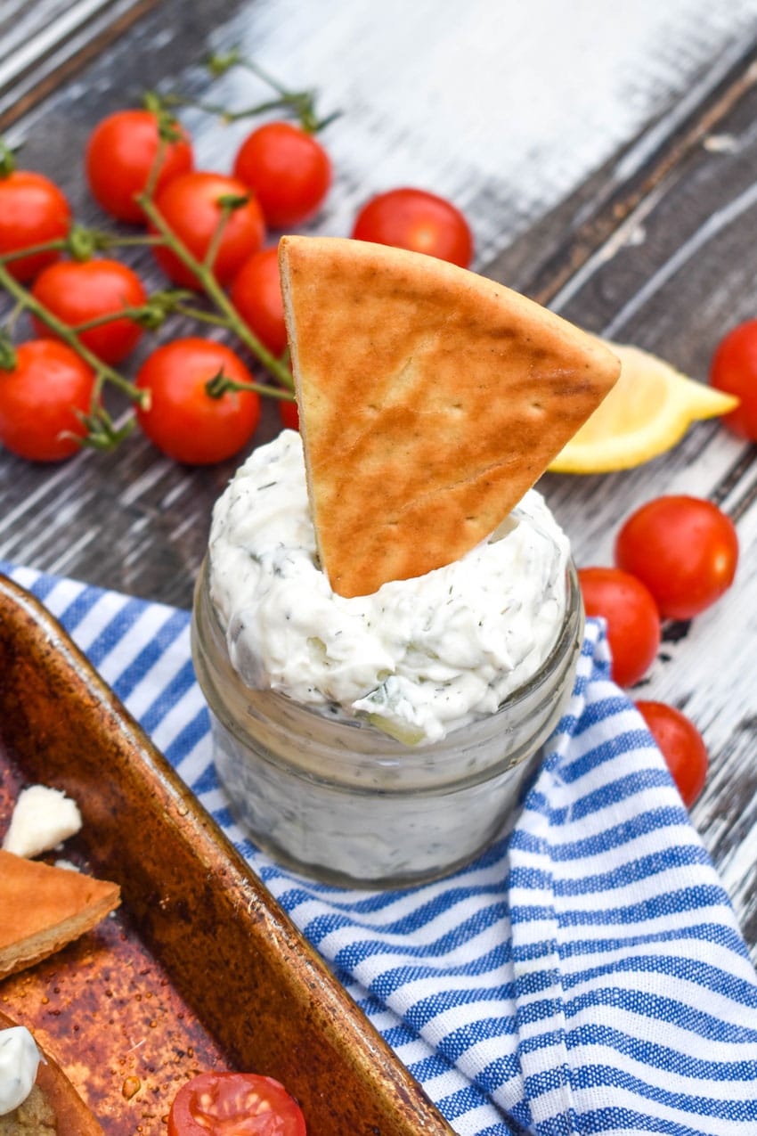 a baked pita chip in a glass jar filled with homemade tzatziki sauce