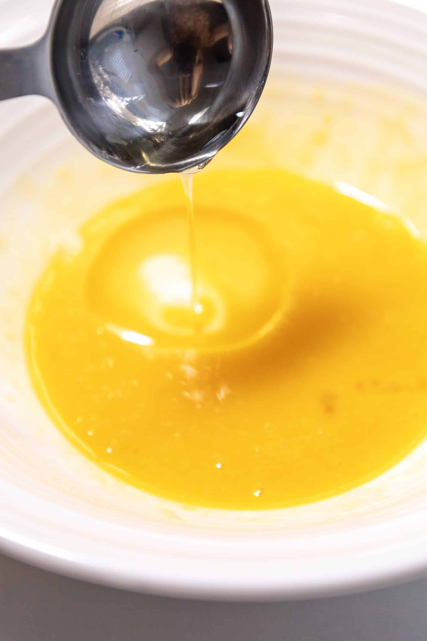 a tablespoon pouring oil into a beaten egg mixture in a mixing bowl