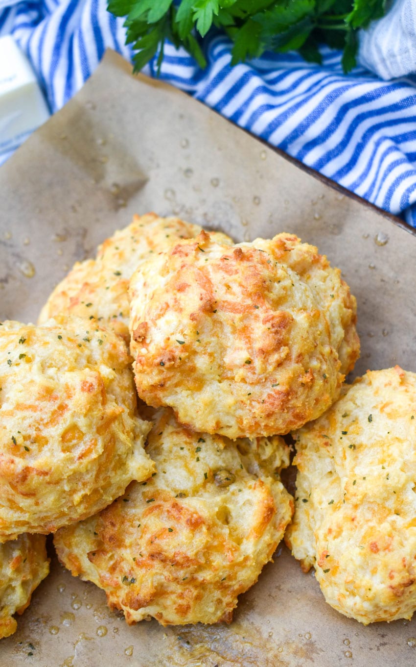a pile of homemade cheddar bay biscuits on a brown parchment paper lined baking sheet
