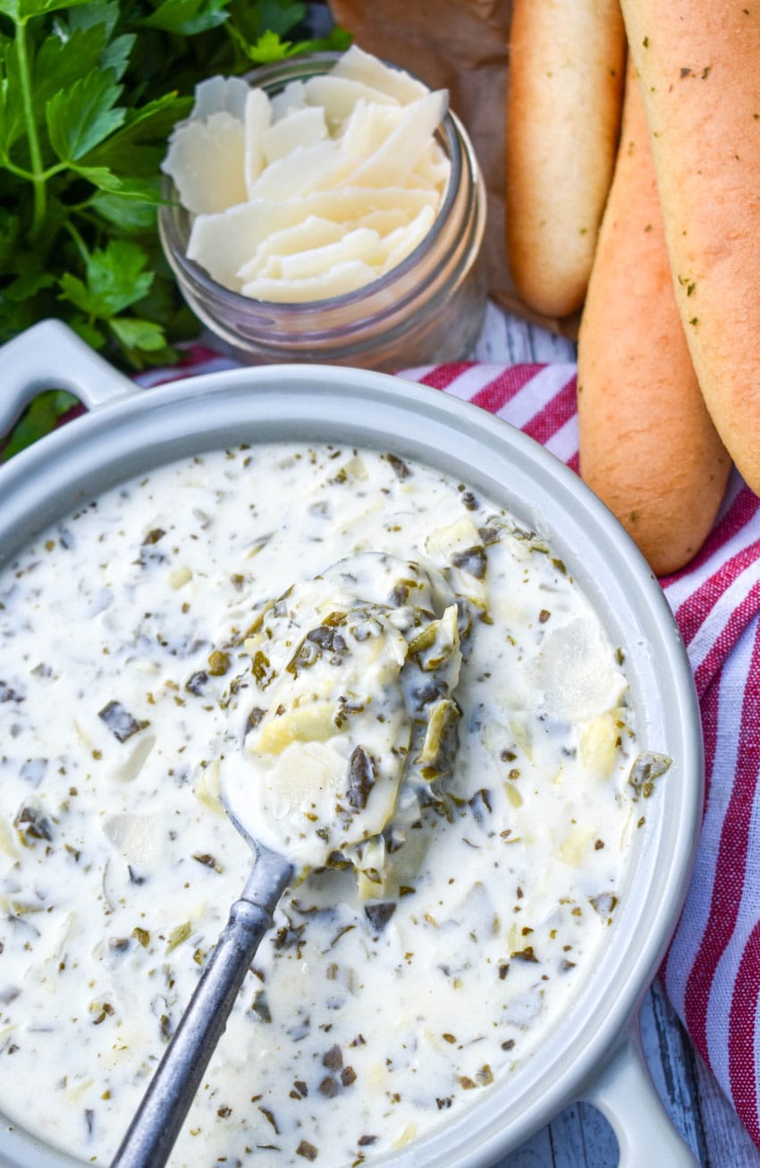 a spoon scooping creamy spinach artichoke soup out of a gray bowl