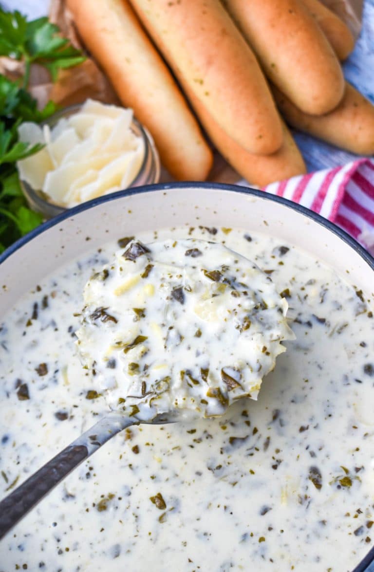 a silver ladle scooping creamy spinach artichoke soup out of a white pot